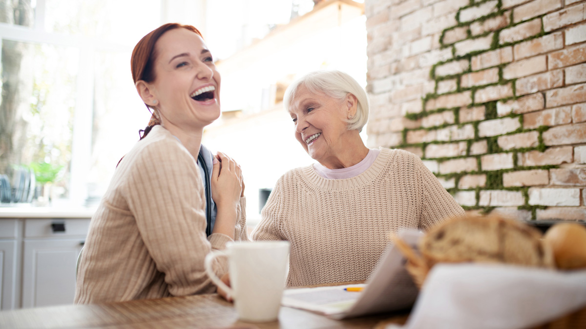 Red-haired caregiver laughing while pensioner joking